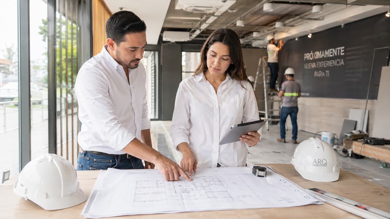 Dos arquitectos en El Salvador revisan planos sobre una mesa, colaborando en un proyecto de construcción.